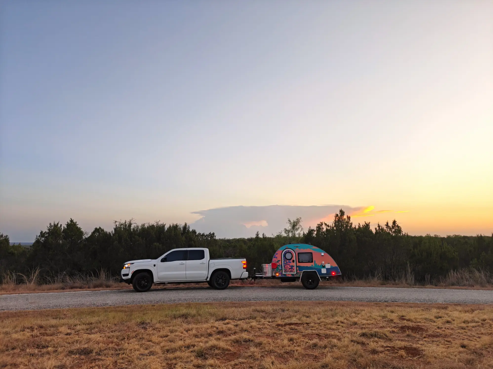Premium glamping teardrop camper campsite at night with warm string lighting under pine trees